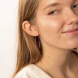 May include: A woman wearing a gold hoop earring and a gold chain necklace. The earring is a thin, curved wire.
