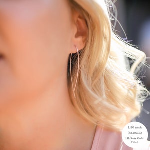 May include: A pair of 1.50 inch (38.10 mm) rose gold filled earrings. The earrings are thin and delicate, with a simple, minimalist design.