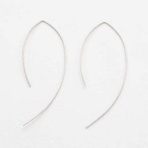 May include: A pair of silver-toned earrings featuring a curved, elongated leaf-like shape. Each earring is constructed from a single thin metal wire that forms a pointed arch at the top and extends into a sweeping, asymmetrical arc at the bottom.