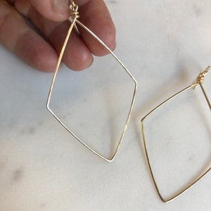 May include: A pair of gold-toned geometric hoop earrings. The earrings are made of thin wire and are shaped like diamonds.