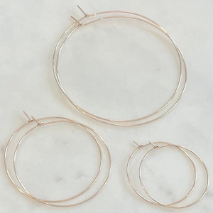 May include: Three gold hoop earrings of different sizes. The largest hoop is about 3 inches in diameter, the middle hoop is about 2 inches in diameter, and the smallest hoop is about 1 inch in diameter.