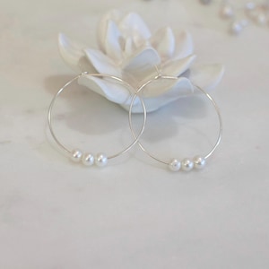 May include: Silver hoop earrings with three white pearls on each hoop.