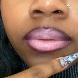 Op de afbeelding: Close-up van een gezicht met een neuspiercing en roze lippenstift. De persoon draagt een zwart-wit gestreept shirt en heeft een vingernagel met een vlinderontwerp.