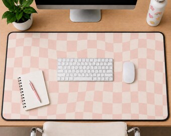 May include: A rectangular desk mat featuring a wavy, distorted checkerboard pattern in alternating shades of light pink and cream. The mat has a black border and is positioned under a white computer keyboard, a white computer mouse, and a spiral notebook.
