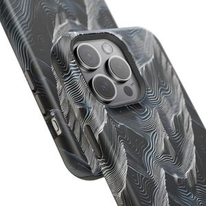 May include: Close-up of a black phone case with a topographic pattern in shades of gray and white. The case has a camera cutout with multiple lenses and buttons on the side. The design resembles a detailed map.