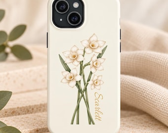 May include: A cream-colored phone case featuring a botanical illustration of a bouquet of white and pale yellow daffodils with green stems. The name Scarlett is printed in a gold cursive script vertically along the right side of the flowers.