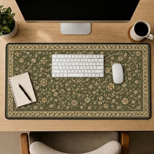 May include: A rectangular desk mat featuring an olive green background with a repeating cream and tan floral pattern and a decorative border. The mat is positioned on a wooden desk surface beneath a white computer keyboard and mouse.