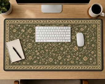 May include: A rectangular desk mat featuring an olive green background with a repeating cream and tan floral pattern and a decorative border. The mat is positioned on a wooden desk surface beneath a white computer keyboard and mouse.
