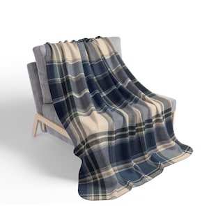 May include: A soft throw blanket featuring a classic plaid pattern in shades of navy blue, light blue, and cream. The fabric displays a woven texture with intersecting horizontal and vertical lines, creating a balanced grid design across the surface.