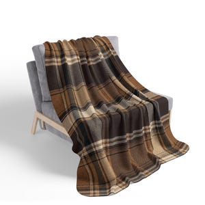 May include: A woven throw blanket featuring a plaid pattern in shades of dark brown, tan, and cream. The blanket is draped over a gray upholstered chair with light-colored wooden legs, showcasing a textured fabric with intersecting lines.