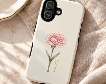 May include: A cream-colored phone case featuring a central illustration of a pink carnation flower with green leaves and stem. The name Victoria is printed in a gold script font vertically alongside the flower stem. The case has a black camera cutout.