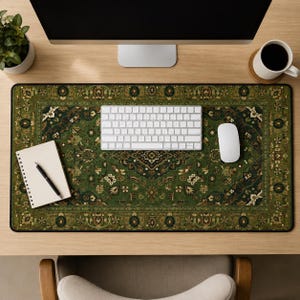 May include: A rectangular desk mat featuring a detailed green, black, and cream-colored ornate pattern reminiscent of a traditional rug. The mat is positioned under a white computer keyboard, a white computer mouse, and a spiral-bound notebook with a pen.