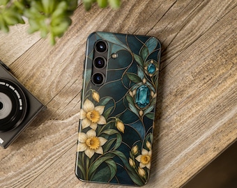 Puede incluir: Una funda para smartphone con un patrón de vidrieras en azul cerceta oscuro, flores de narciso amarillas y detalles de gemas azules. El diseño incluye finas líneas doradas que separan los segmentos y una triple lente de cámara visible.