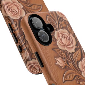 May include: A tan phone case featuring a raised, embossed floral pattern of roses and leaves. The case has a black camera lens housing and black side buttons. The design covers the back and sides of the case, showing a textured, leather-like surface.