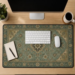 Op de afbeelding: Een rechthoekige bureaumat met een gedetailleerd saliegroen en beige bloemenpatroon dat doet denken aan een traditioneel tapijt. De mat heeft een donkere rand en biedt een ondergrond voor een wit computertoetsenbord, een witte muis en een notitieblok.