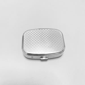 May include: A silver pill box with a patterned lid. The lid has a diamond pattern.