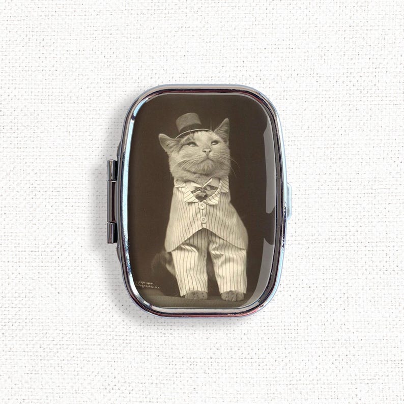 May include: A vintage-style photo of a cat wearing a top hat and a tuxedo, printed on a silver compact mirror.