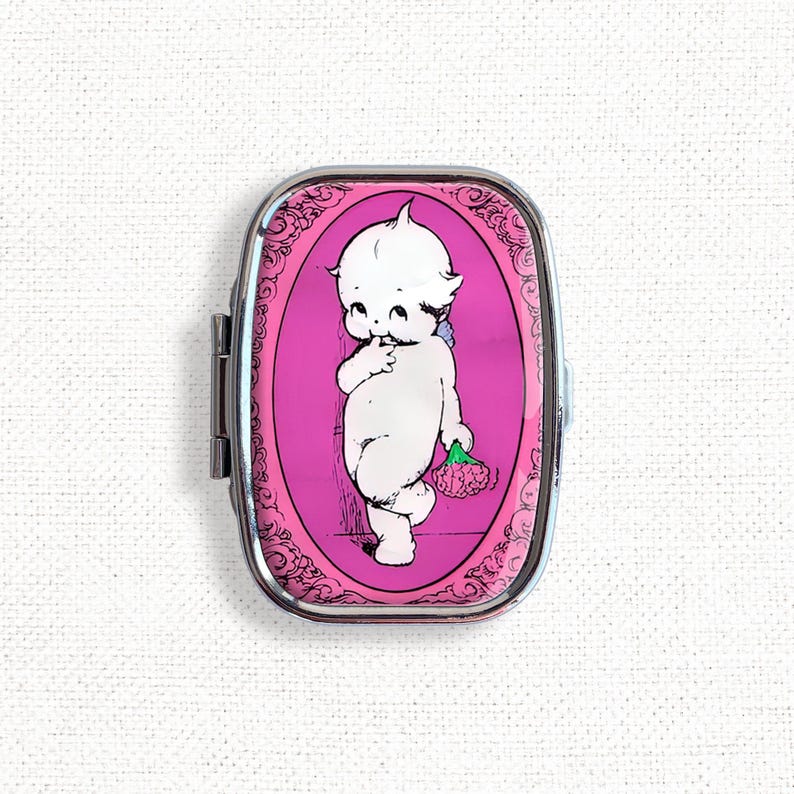 May include: A silver compact mirror with a pink background and a black and white illustration of a cherub holding a flower.