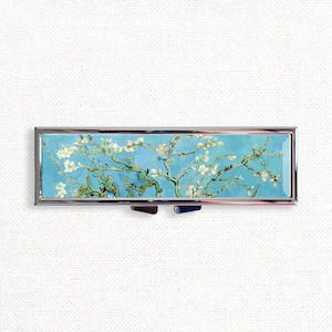 May include: A silver pill box with a hinged lid featuring a reproduction of Vincent van Gogh's painting "Almond Blossom".