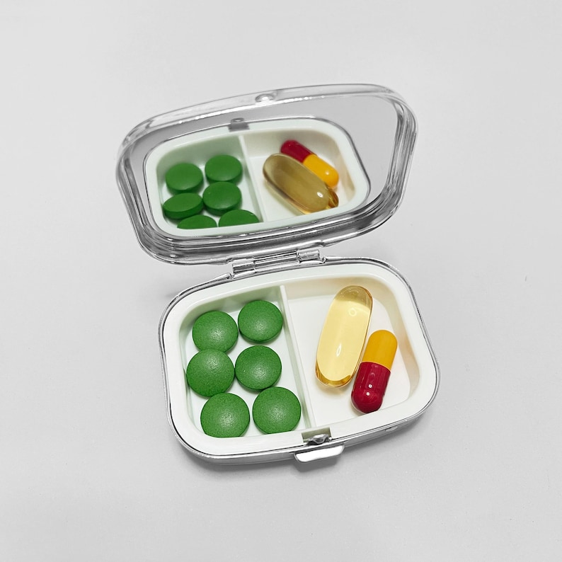 May include: A silver pill box with a mirror lid. The box has two compartments, one with green pills and the other with yellow and red pills.