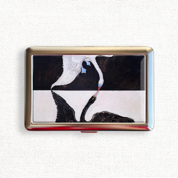 May include: A metal cigarette case with a black and white image of two swans, one white and one black, facing each other.