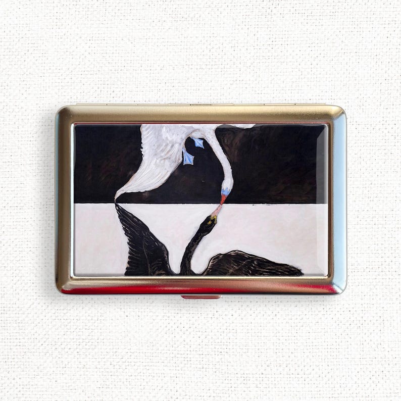 May include: A metal cigarette case with a black and white image of two swans, one white and one black, facing each other.