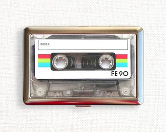 May include: A silver cassette tape case with a clear plastic window showing a blank cassette tape. The tape has the text "INDEX" and "FE 90" printed on it. The tape has a rainbow colored stripe.