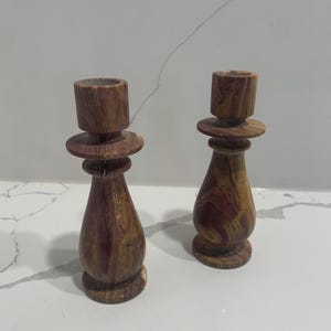 Puede incluir: Dos candelabros de madera con un patrón de mármol marrón y rojo. Los candelabros tienen una base ancha y una parte superior estrecha.