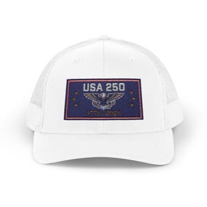 Puede incluir: Gorra de camionero blanca con parte trasera de malla y visera curva. La parte delantera presenta un parche rectangular con el texto "USA 250" sobre un emblema de águila y las fechas "1776-2026". El parche tiene un fondo azul marino con estrellas doradas.