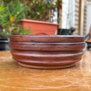 May include: A brown ceramic bowl with a textured, ribbed design. The bowl has a slightly rounded shape and a wide rim.