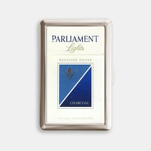 May include: A silver cigarette case holding a pack of Parliament Lights cigarettes. The pack is white with blue text and a blue and black diagonal design. The text "RECESSED FILTER" and "CHARCOAL" are also visible.