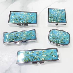 May include: Set of five silver pill boxes with a blue and white floral design. The boxes are rectangular and have a hinged lid.