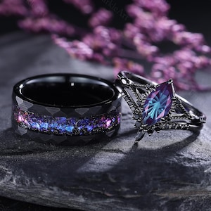 Può includere: Due anelli neri. Uno presenta un design simile a una galassia con sfumature blu, viola e rosa. L'altro anello ha una gemma taglio marquise con colori verde acqua e viola. Gli anelli sono su una pietra grigio scuro.