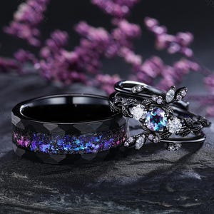 Könnte beinhalten: Ein schwarzer Ehering mit einem blauen und violetten Galaxie-Design und ein schwarzer Ring mit einem Blatt-Design und einem großen, schillernden Edelstein.