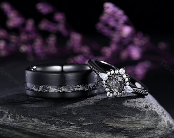 Może przedstawiać: Czarna obrączka ślubna z cienką linią białych diamentów i czarny pierścionek zaręczynowy z diamentem w otoczeniu białych diamentów.