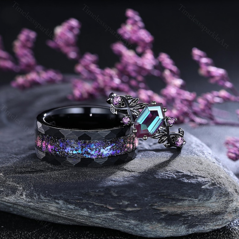 May include: Two rings, one black with a textured band and a colourful, galaxy-like inlay. The other ring is black with a large, emerald-cut, teal and purple gemstone, accented with small pink stones and a floral design.