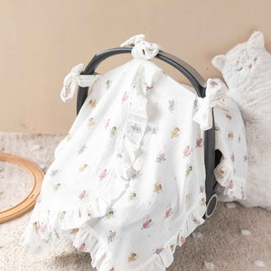 May include: White muslin baby car seat canopy with a frilled trim and a fairy print. The canopy has ties to attach to the car seat.
