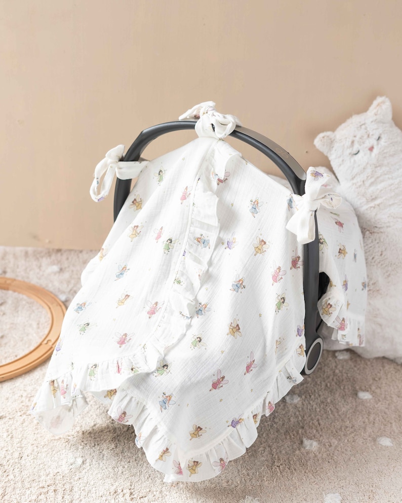 May include: White muslin baby car seat canopy with a frilled trim and a fairy print. The canopy has ties to attach to the car seat.