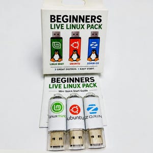 May include: A white box and three USB drives labelled "BEGINNERS LIVE LINUX PACK." The box features the text "LINUX MINT," "UBUNTU," and "ZORIN OS" with penguin graphics. The USB drives are white with the same logos and text.
