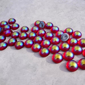 May include: A scattering of iridescent glass gems. Each gem is a vibrant red with a shimmering, multi-coloured surface that reflects yellow, blue, and purple hues. Some gems are cut in half, revealing a swirling pattern.