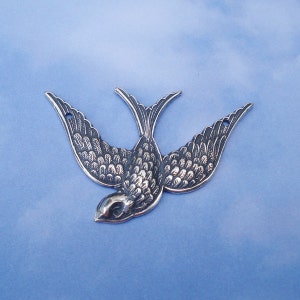 May include: A silver-toned metal swallow charm with detailed feather markings. The swallow is in flight with its wings spread wide.