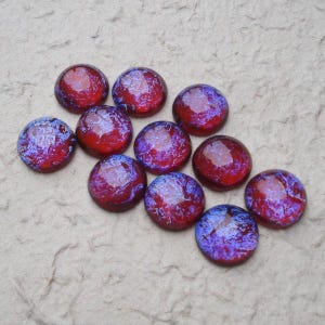 May include: A collection of eleven circular glass cabochons featuring a vibrant color palette of deep red and purple with a swirling, marbled texture. Each piece has a smooth, domed surface that reflects light, creating a glossy finish.