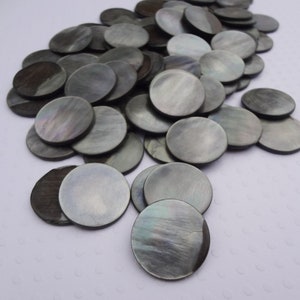 May include: A pile of round, black mother of pearl shell discs. The discs are smooth and have a slight iridescent sheen.