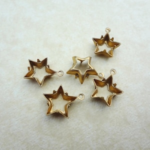May include: Five gold-coloured star charms with a hollow centre and a small loop at the top for attaching to jewellery. The stars have a textured surface and are arranged on a cream-coloured background.