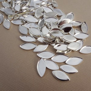 May include: A large pile of silver-colored metal leaf-shaped embellishments. The embellishments are scattered on a brown surface.