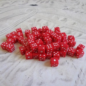 May include: A collection of red dice with white dots scattered on a light-colored surface. The dice are small, square, and have varying numbers of dots on each face, indicating their value. The image showcases a variety of dice, perfect for board games or tabletop gaming.