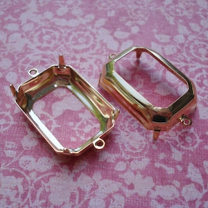 May include: Two gold-tone metal settings for rectangular cabochons. Each setting has four prongs and two loops for attaching a chain or cord.