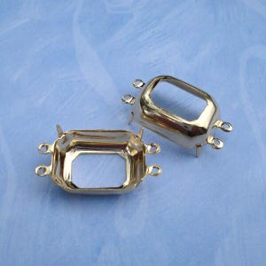 May include: Two gold-toned metal jewelry settings with a rectangular, open-center design. Each setting features four small prongs on the corners and two small loops on each of the shorter sides, intended for connecting to other jewelry components.