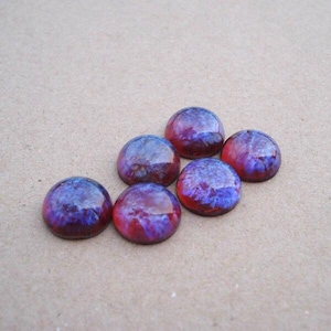 May include: Six circular cabochons with a smooth, domed surface. Each piece features a swirling, marbled pattern of deep purple, vibrant blue, and reddish-pink hues, creating a glossy, reflective appearance across the set of small, round items.