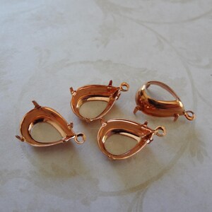 May include: Four copper-coloured teardrop-shaped pendant settings with a smooth, shiny finish. The settings are designed to hold a cabochon stone.